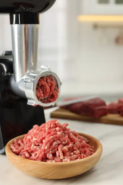 Electric meat grinder with minced beef on white marble table indoors