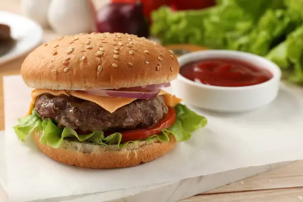 Tasty hamburger with patty, cheese and vegetables on light table, closeup