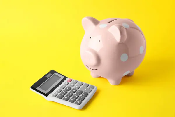 Calculator and pink piggy bank on yellow background