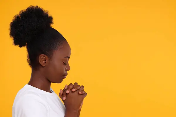Woman with clasped hands praying to God on orange background. Space for text