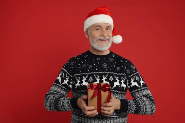 Kırmızı arka planda Noel süveteri ve Noel Baba şapkası taşıyan son sınıf öğrencisi.