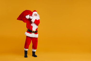 Noel Baba turuncu arka planda Noel hediyeleriyle dolu bir çanta, mesaj için boşluk