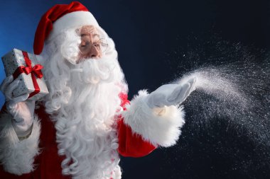 Noel hediyeli Noel Baba koyu mavi arka planda kar üflüyor