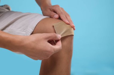 Adam açık mavi arka planda dizine sıva yapıştırıyor, yakın plan. Metin için boşluk