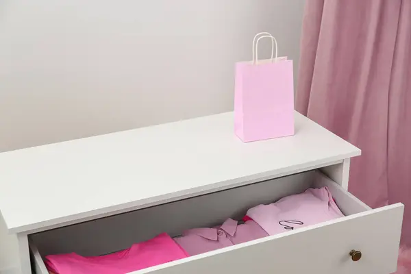 White chest of drawers with pink clothes and bag indoors