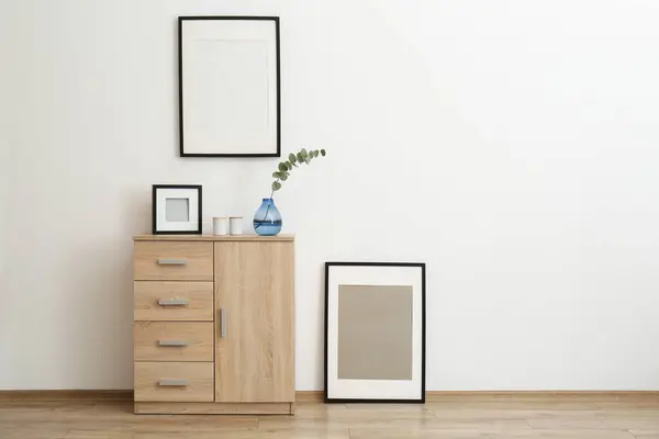 Wooden cabinet and photo frames in room with white wall, space for text. Interior design