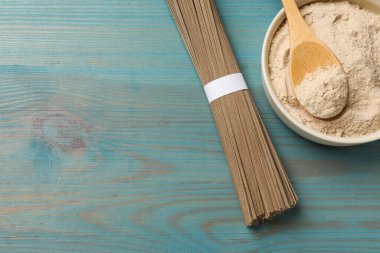 Pişmemiş karabuğday eriştesi (soba) ve açık mavi ahşap masa üzerinde un, üst manzara. Metin için boşluk