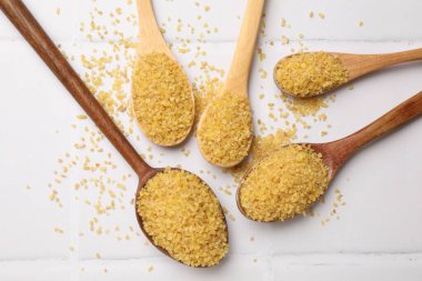 Beyaz döşeme üzerinde çiğ bulgur ile kaşıklar düz yatıyordu.