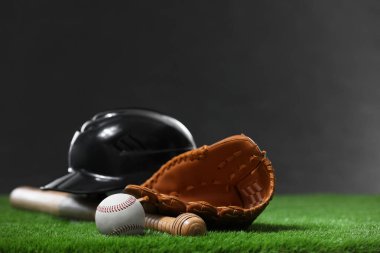 Beyzbol sopası, beysbol kaskı, deri eldiven ve yeşil çimlerin üzerinde koyu arka planda duran top. Metin için boşluk