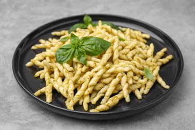 Pesto soslu lezzetli trofie makarna ve açık gri masada fesleğen yaprağı.