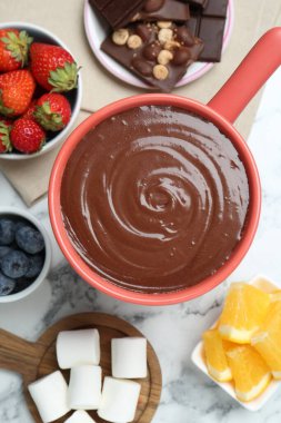 Erimiş çikolatalı fondü kabı, marşmelov, taze portakal ve beyaz mermer masada farklı meyveler, düz uzanmış.