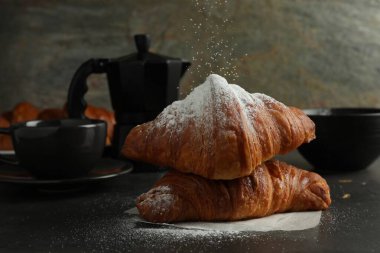 Gri masadaki taze kruvasanların üzerine toz şekeri serpiyorum.