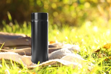 Black thermos and blanket on green grass outdoors, space for text clipart