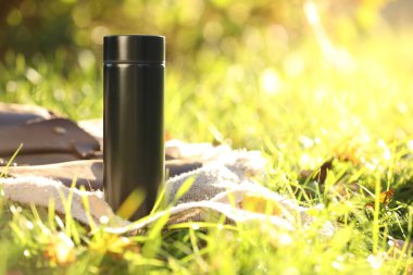 Black thermos and blanket on green grass outdoors, space for text clipart
