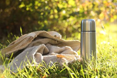 Metal thermos and bag with blanket on green grass outdoors clipart