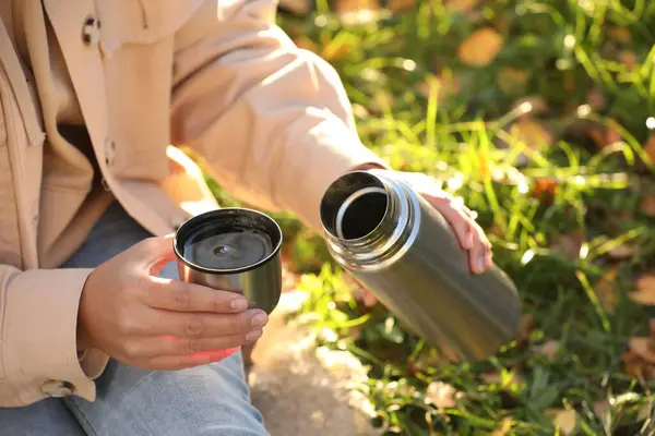Woman with thermos and cup lid on green grass outdoors, closeup