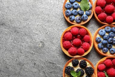 Açık gri masada farklı taze böğürtlenli turtalar, düz yatış ve metin için boşluk. Tatlı nefis.