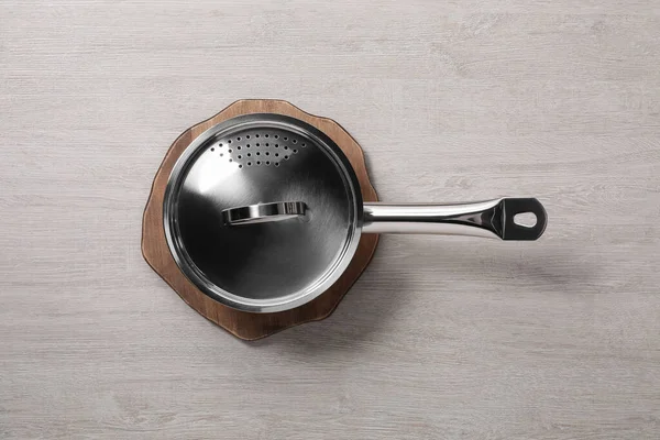 Steel saucepan with strainer lid on light wooden table, top view