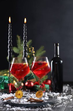 Gözlüklü Noel Sangria kokteyli, yanan mumlar ve siyah ahşap masada kar.