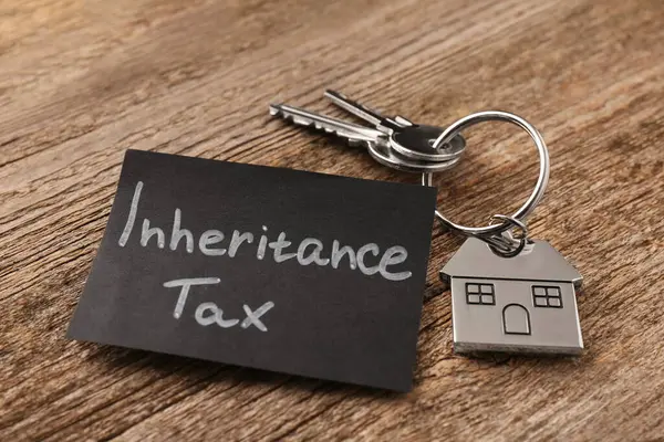 Inheritance Tax. Card and keys with key chain in shape of house on wooden table, closeup