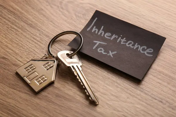 Inheritance Tax. Card and key with key chain in shape of house on wooden table, closeup