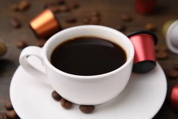 Cup of coffee, capsules and beans on table, closeup