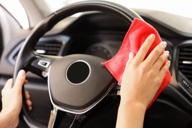Arabasında bez parçasıyla direksiyonu temizleyen kadın, yakın plan.