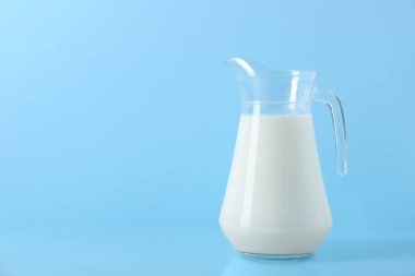 Açık mavi arkaplanda bir sürahi taze süt, metin için boşluk