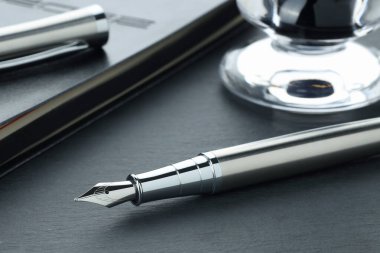 Gri desenli masa üzerindeki çeşme kalem ve defter, yakın plan.