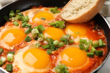 Lezzetli Shakshuka kızartma tavasında ve ekmek parçası masada, yakın plan.