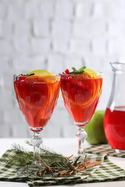 Christmas Sangria cocktail in glasses, cinnamon sticks and fir tree branch on white table against brick wall