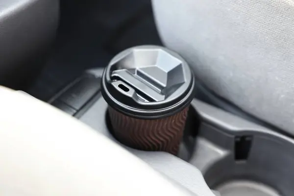 Coffee to go. Paper cup with tasty drink in holder inside of car, closeup