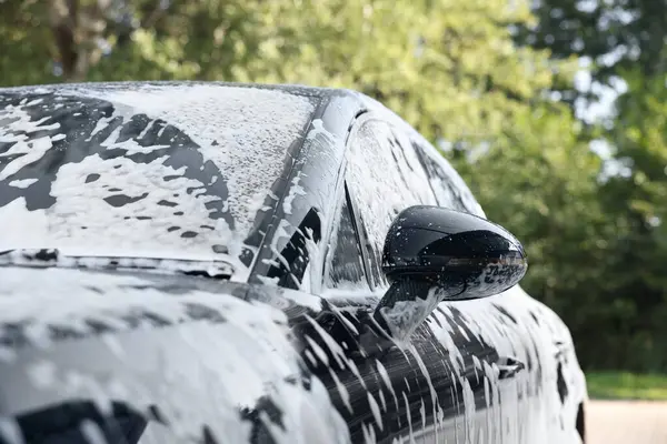 Auto covered with cleaning foam at outdoor car wash, closeup