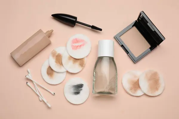 Bottle of makeup remover, dirty cotton pads, buds and different cosmetic products on beige background, flat lay