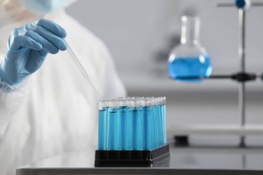 Scientist taking sample of light blue liquid in laboratory, closeup