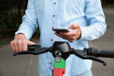 Akıllı telefonu kullanan bir adam açık havada elektrikli scooter 'ın önünü açar ve öder.
