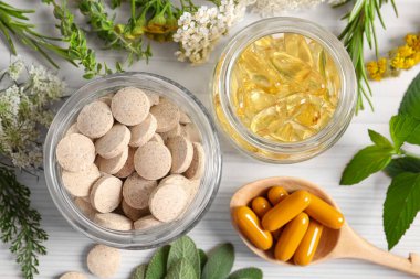 Farklı haplar, çiçekler ve otlar beyaz ahşap masa, düz yatak. Beslenme takviyeleri