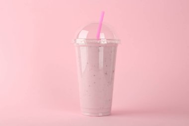 Pembe arka planda plastik bir bardak lezzetli smoothie.