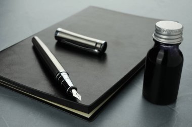 Şık dolmakalem, bir şişe mürekkep ve gri desenli masa üzerindeki deri defter, yakın plan.
