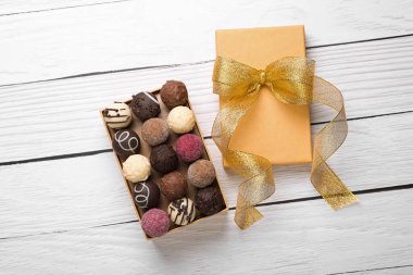 Beyaz ahşap masanın üstünde nefis çikolata şekerleri olan bir kutu aç.