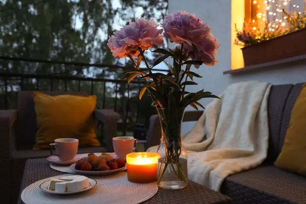 Rattan table with drink, food, flowers and candle on outdoor terrace in evening