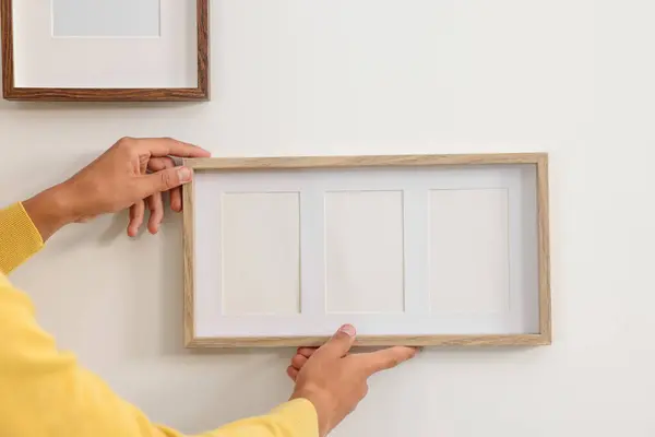 Young man hanging picture frames on white wall indoors, closeup. Space for text