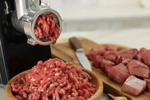 Electric meat grinder with beef on white table, closeup. Space for text