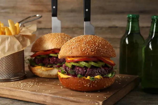 Tasty vegetarian burgers served with french fries and beer on wooden table