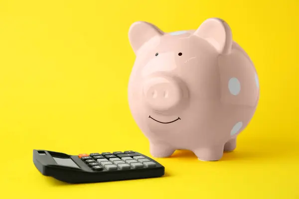 Calculator and pink piggy bank on yellow background