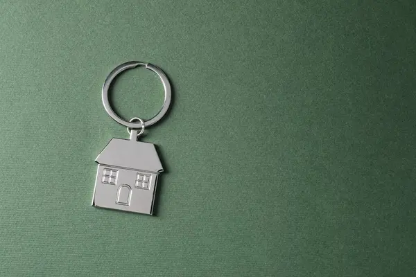 Metallic keychain in shape of house on dark green background, top view. Space for text