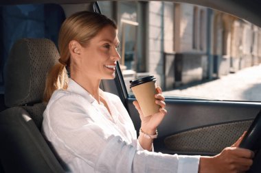 Paket kahve. Kağıt bardakta içen mutlu kadın arabasını sürüyor.
