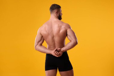 Genç adam turuncu arka planda siyah iç çamaşırı giyiyor. Metin için boşluk