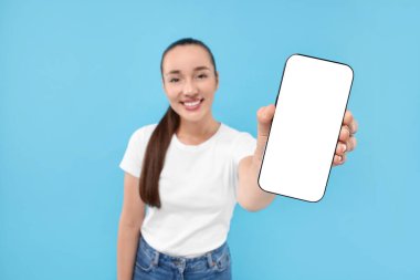 Açık mavi arka planda akıllı telefon gösteren genç bir kadın. Seçici bir odak noktası. Tasarım için model