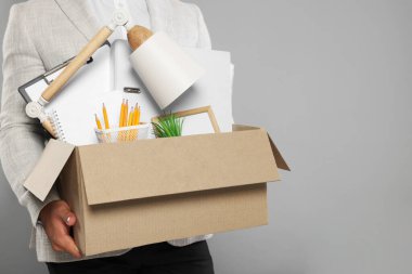 Açık gri arka planda kişisel ofis eşyalarıyla dolu bir kutuya sahip işsiz adam, yakın plan. Metin için boşluk